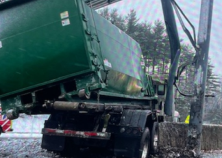 A flatbed truck carrying a dumpster that struck an overhead highway sign structure.